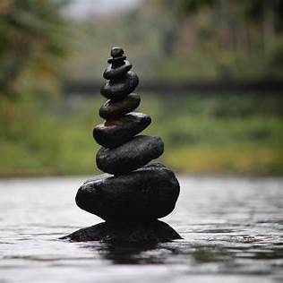 Balanced natural stones stacked peacefully in a calm water setting, symbolising emotional balance and reflection.
