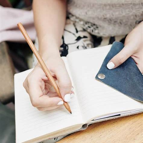 someone writing in a journal using a pencil