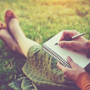Woman sitting crossed legged on a field writing in a journal