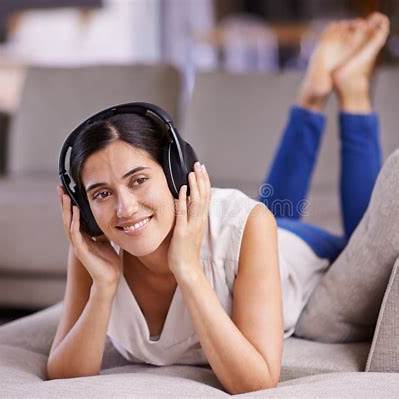 A relaxed person lying on a sofa, wearing headphones, immersed in music and smiling peacefully.