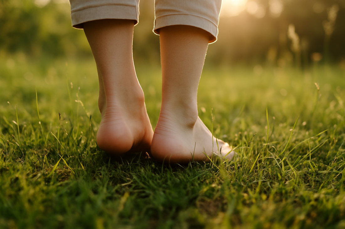 Bare feet of a person standing on sunlit green grass during golden hour, symbolising connection with nature and grounding.