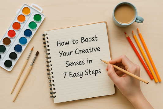 An overhead view of an artist’s desk with a journal, watercolours, paintbrushes, coloured pencils, and a cup of coffee—symbolising a space for creativity and inspiration.